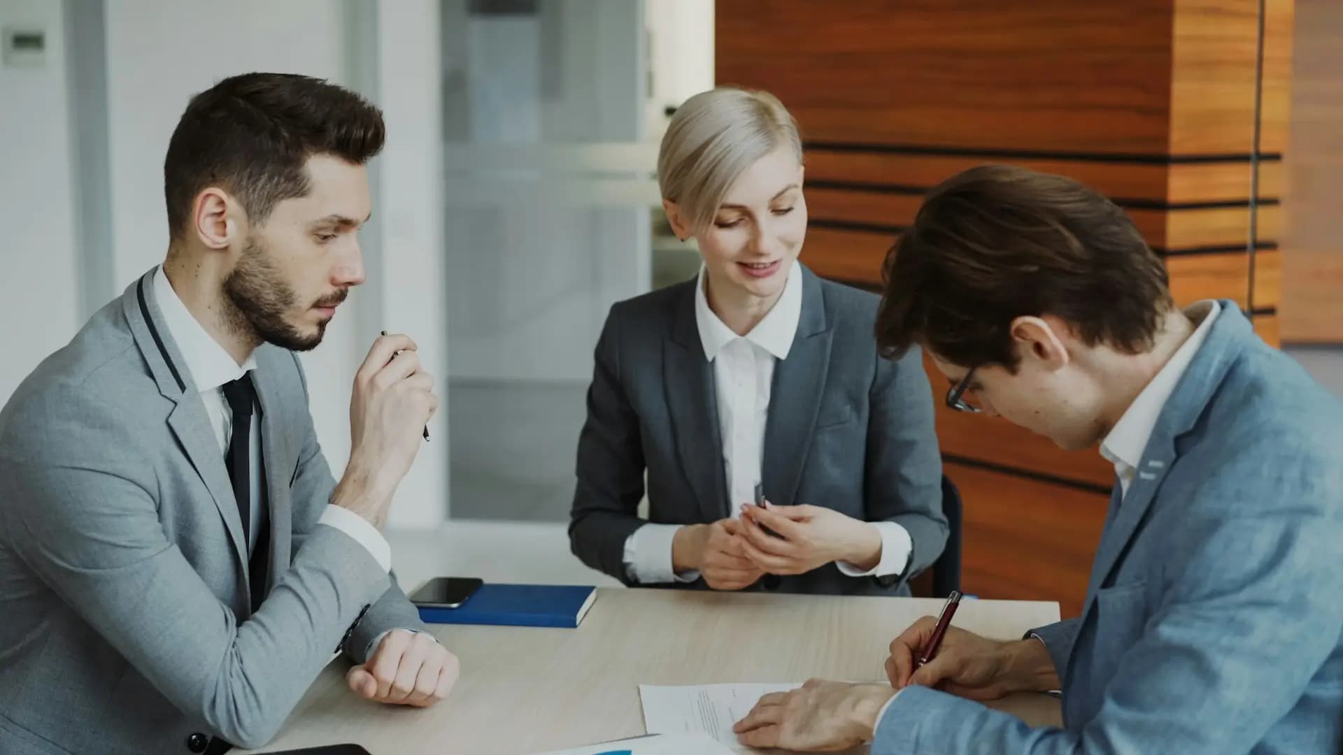 Young businessman in suit signing contract with his colleague while corporate lawyer explaining details of partnership sitting in modern office indoors - Vitaly Gariev, Unsplash