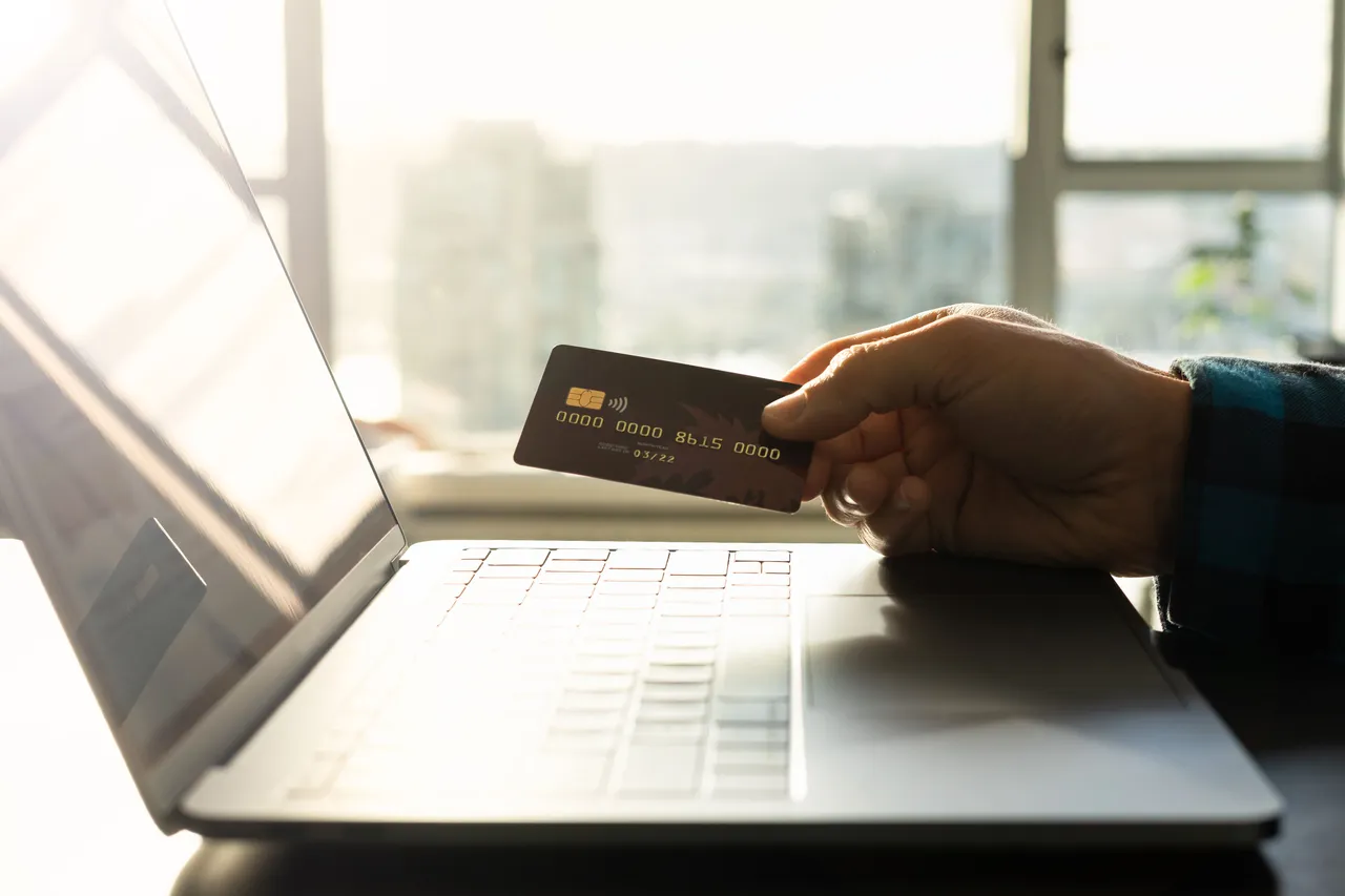 A hand holding a credit card next to a laptop