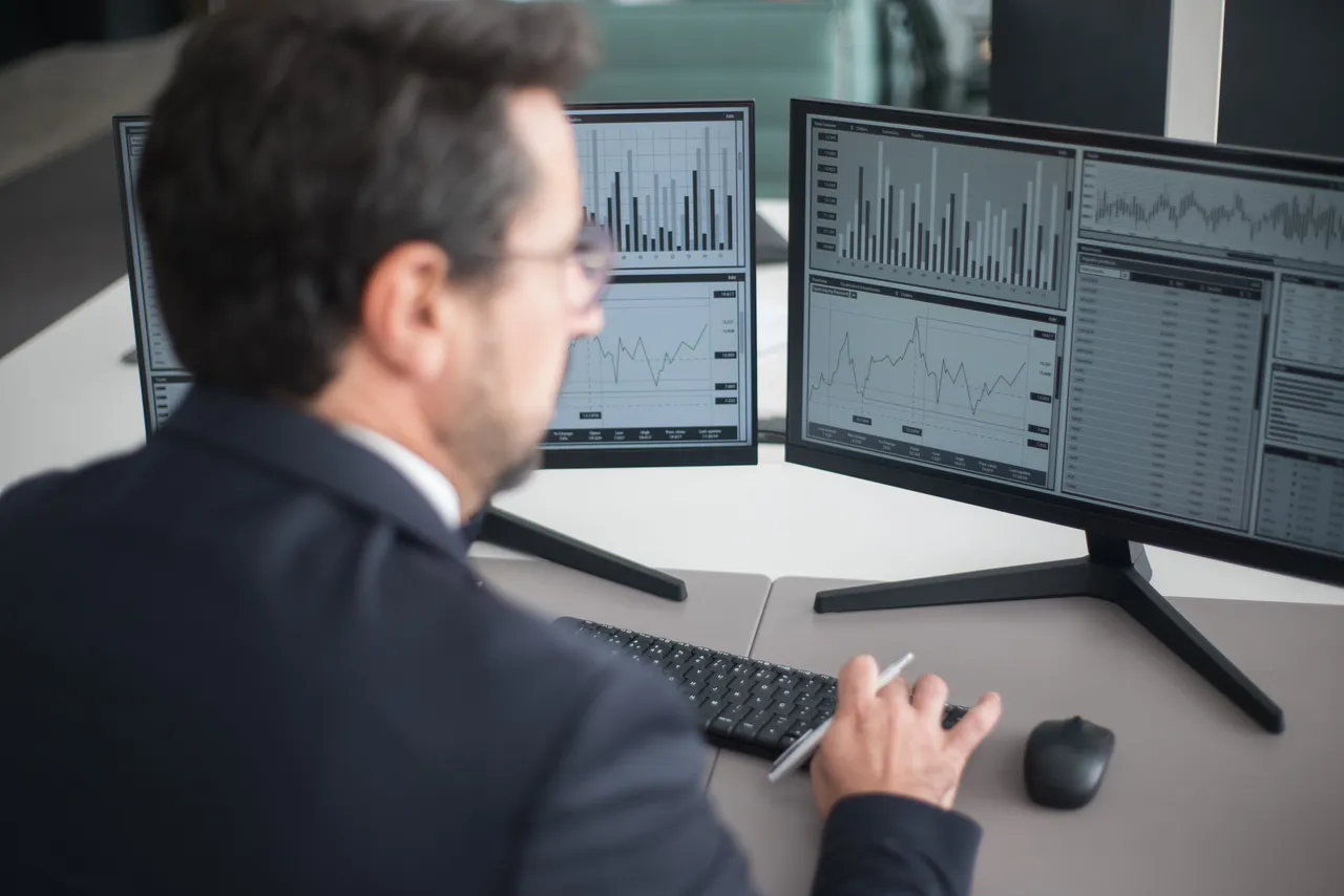 A man in a black suit reviewing financial dashboards on multiple monitors