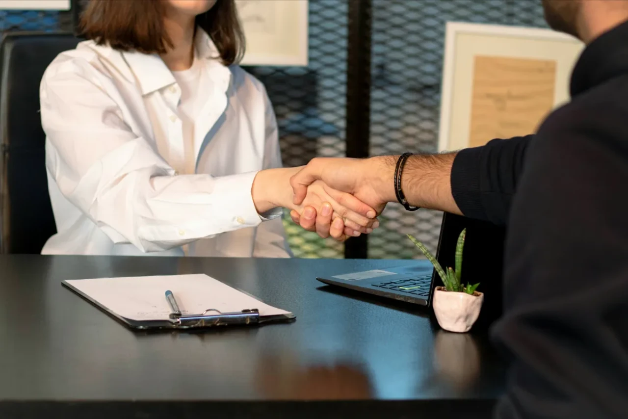A man and a woman shaking hands in front of a laptop